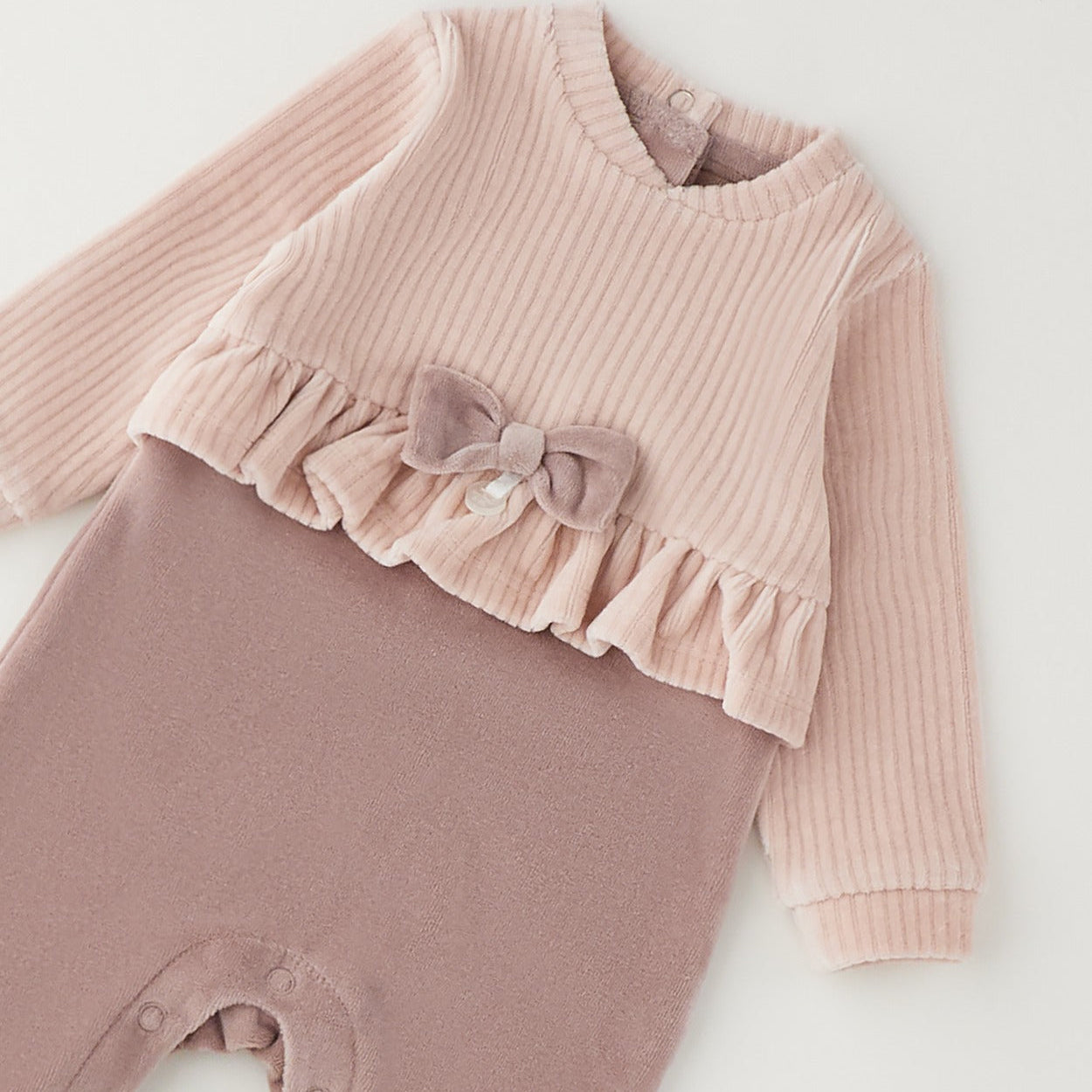 Tutina neonata in ciniglia rosa con fiocco, volant e piedini, ideale per corredino nascita bambina.
