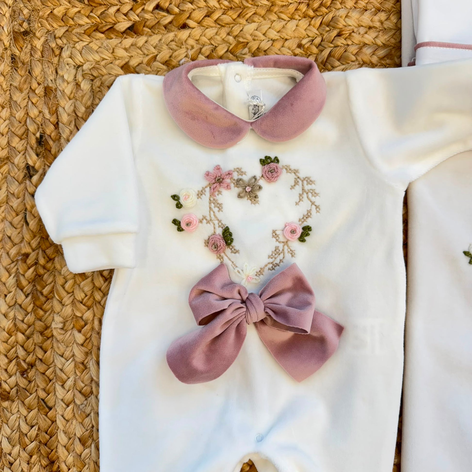 Uscita clinica neonata in ciniglia panna con ricamo floreale a cuore e fiocco rosa composta da tutina, bavetta, cappellino, lenzuola coordinate e copertina sfoderabile.