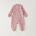 Retro tutina neonata in ciniglia rosa con chiusura a bottoncini e dettaglio a quadretti sui piedini.
