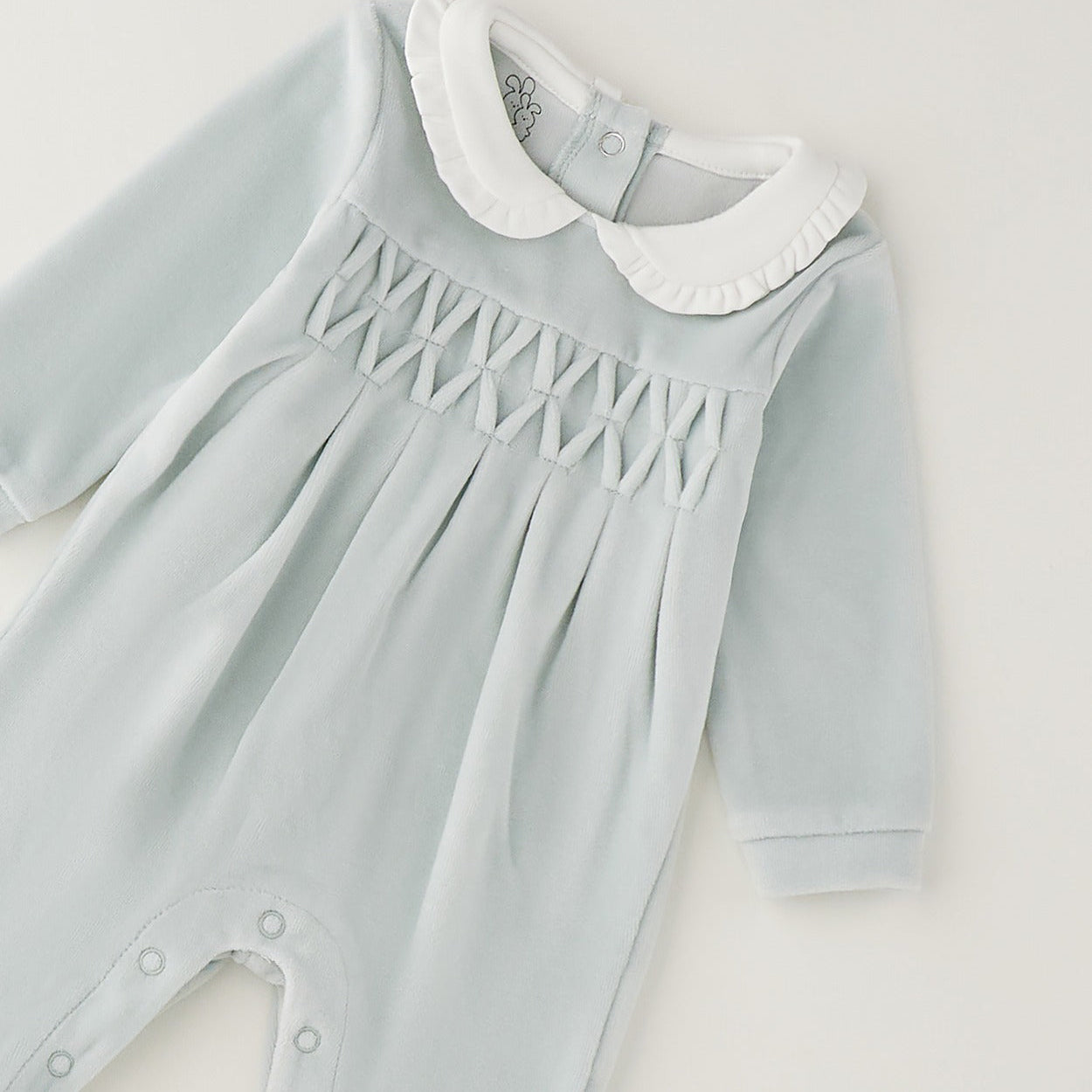 Dettaglio tutina neonata verde menta in ciniglia con colletto bianco e lavorazione smock geometrica