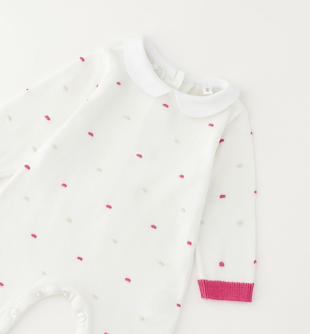 Dettaglio tutina neonata in cotone bianco con colletto e ricami rosa e panna