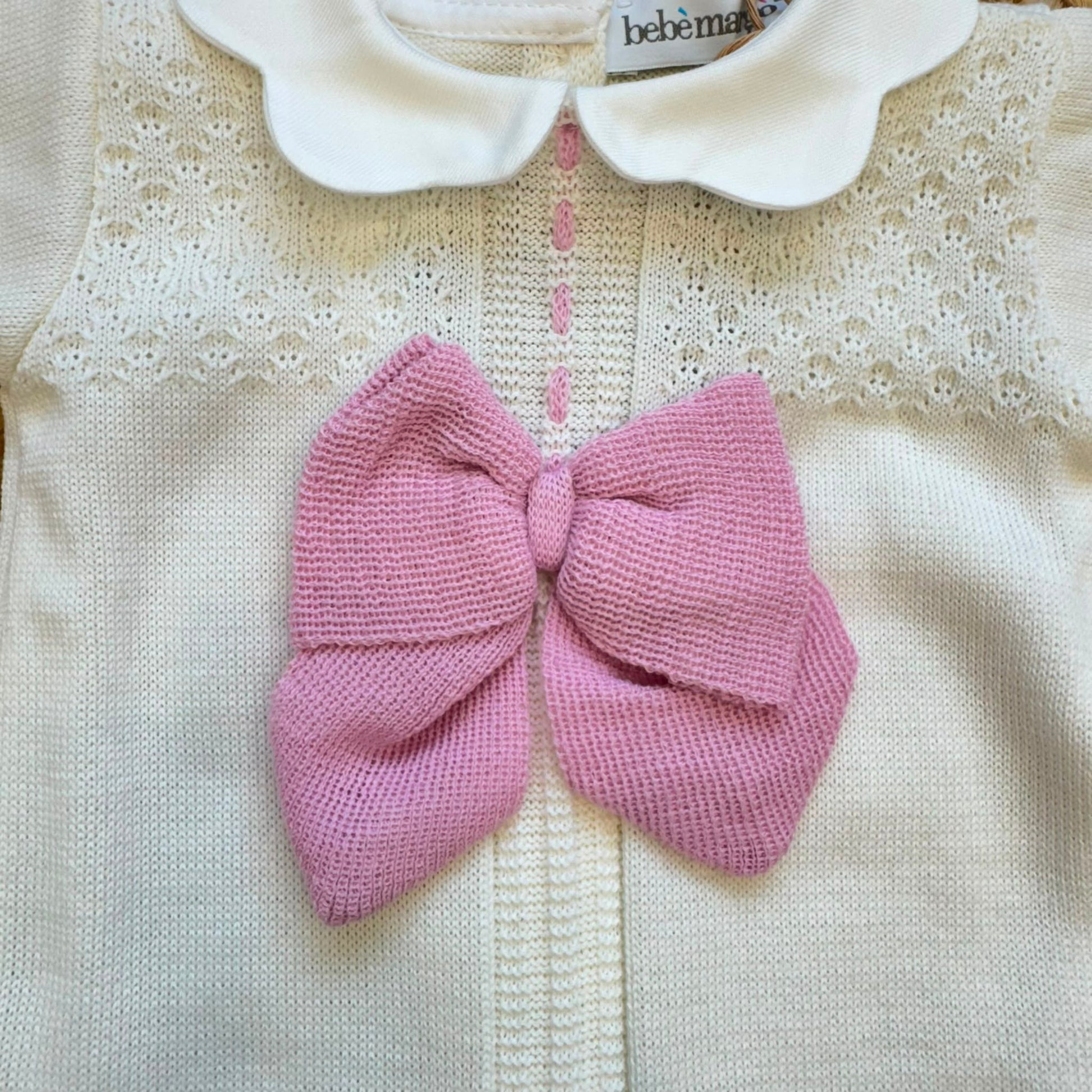 Dettaglio colletto e lavorazione traforata della tutina neonata panna e rosa in lana