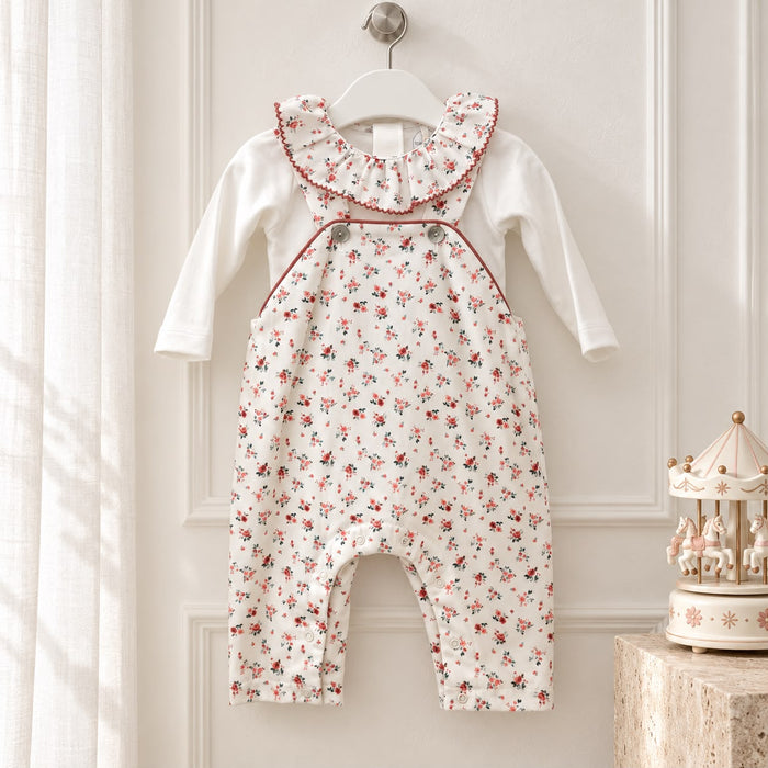 Tutina neonata in cotone con salopette bianca a piccoli fiori rossi e rosa, maglia bianca a maniche lunghe, ampio colletto volant floreale, bottoni sulle bretelle e profili color rosso mattone.