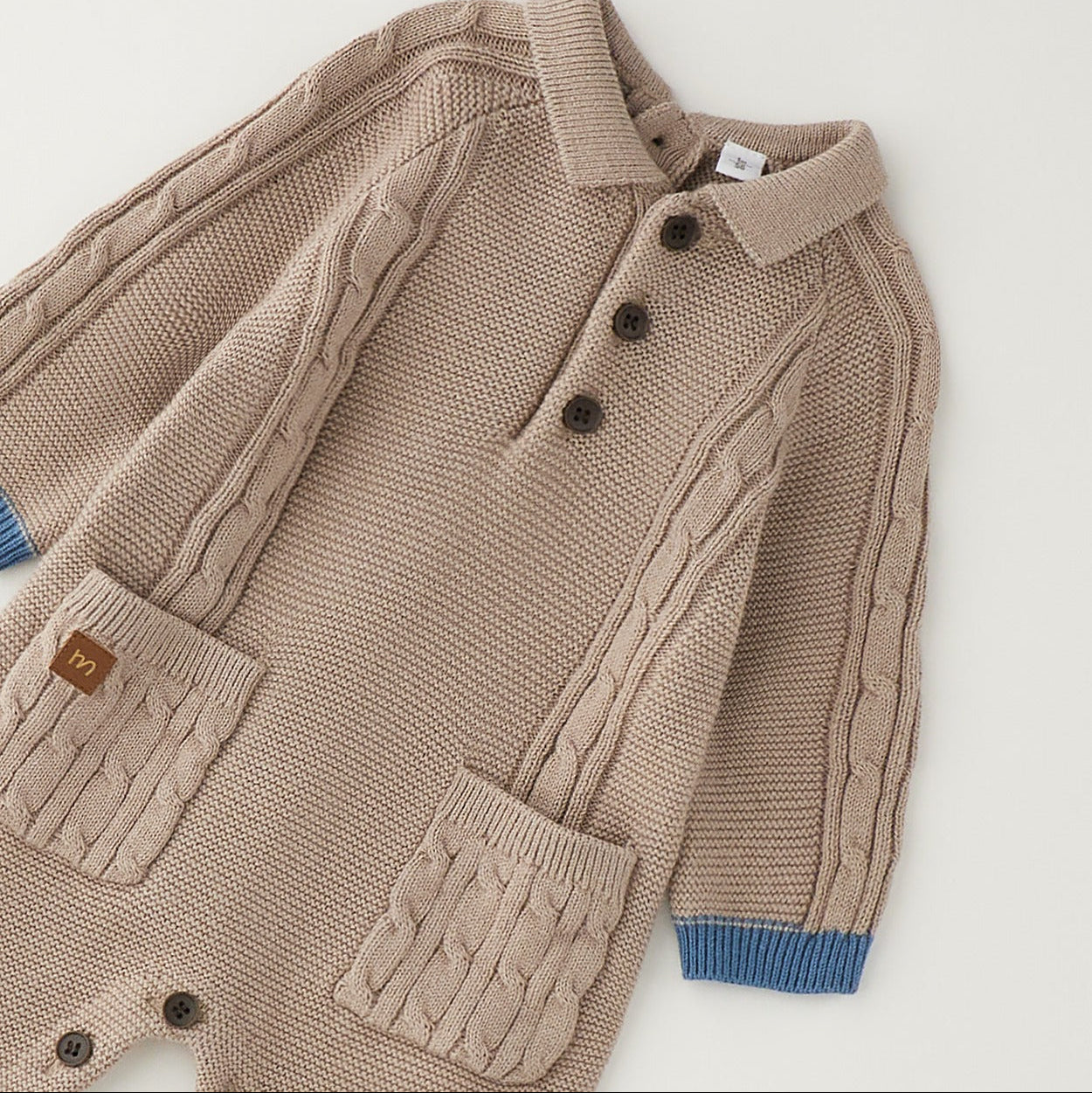 Tutina neonato tricot beige in 80% cotone e 20% lana con trecce, taschine e dettagli petrolio