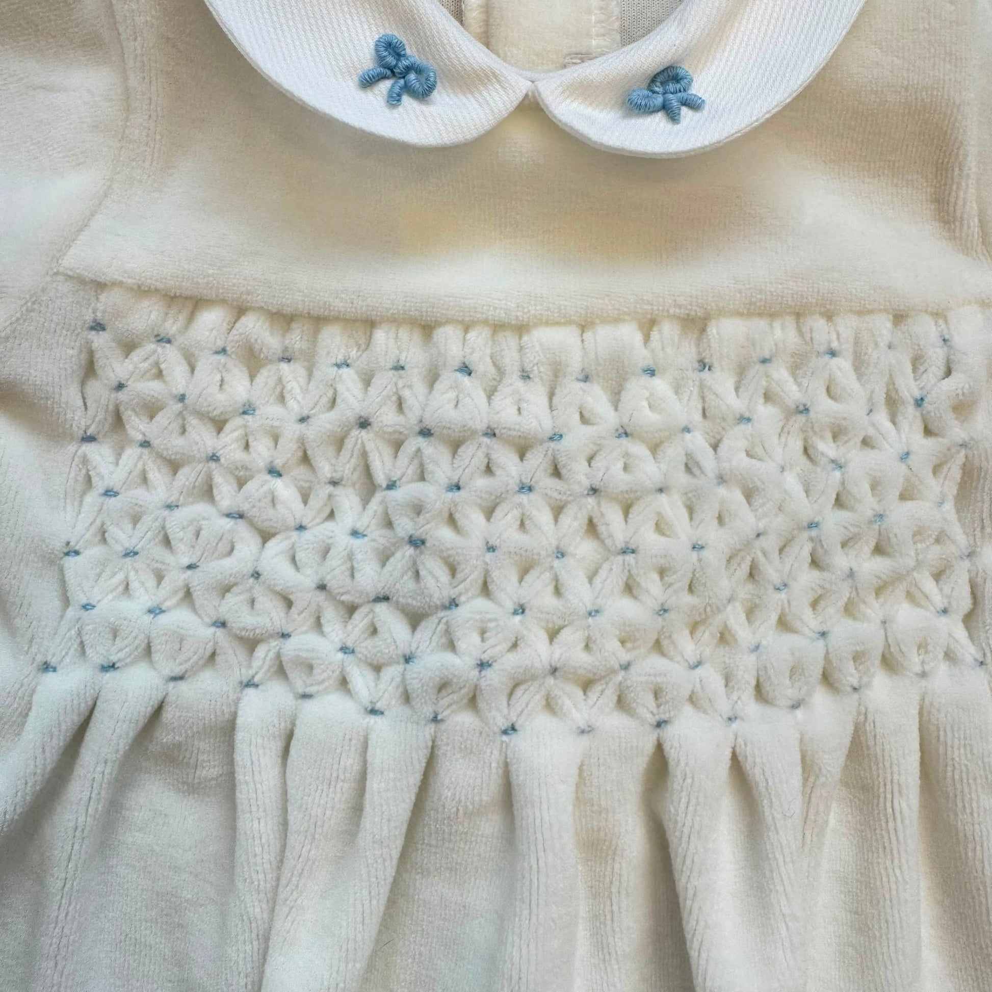 Tutina neonato in ciniglia color cielo con colletto bianco ricamato e fiocchetti.