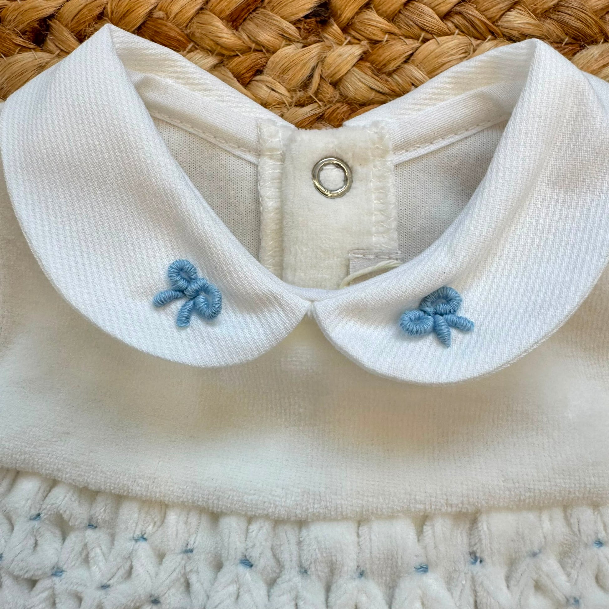 Tutina neonato in ciniglia color cielo con colletto bianco ricamato e fiocchetti.