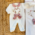 Uscita clinica neonata in ciniglia panna con ricamo floreale a cuore e fiocco rosa composta da tutina, bavetta, cappellino, lenzuola coordinate e copertina sfoderabile.