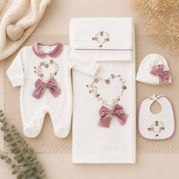 Uscita clinica neonata in ciniglia panna con ricamo floreale a cuore e fiocco rosa composta da tutina, bavetta, cappellino, lenzuola coordinate e copertina sfoderabile.