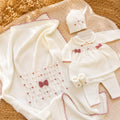 Uscita clinica neonata in pura lana color panna con fiocchetti rosa, colletto bianco, cappellino, scarpine e copertina coordinata.
