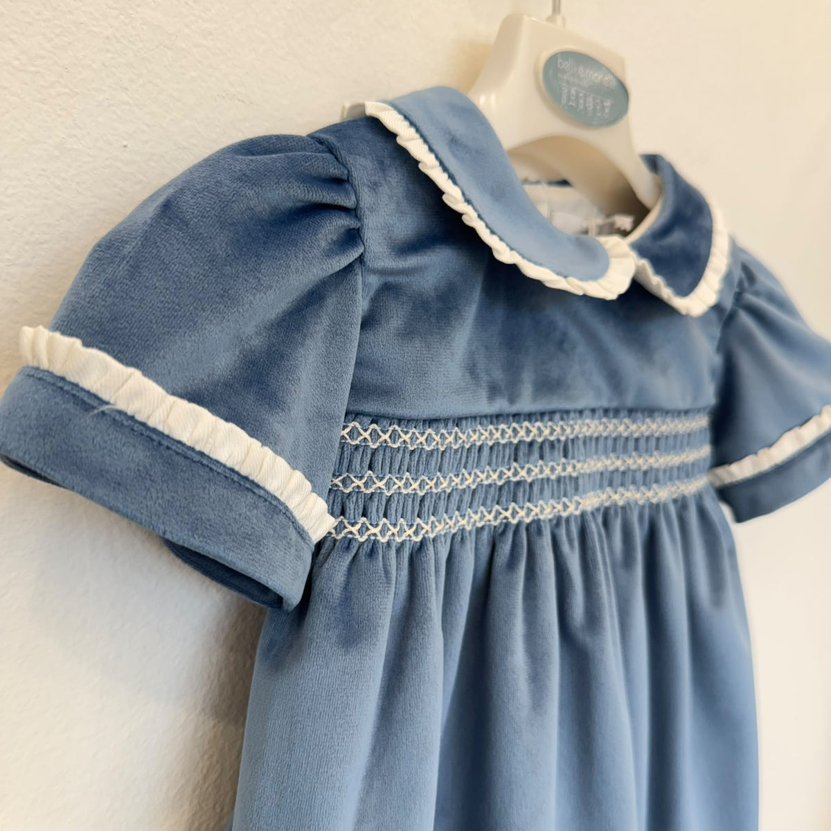 Dettaglio dell'abito bambina in velluto azzurro polvere con lavorazione smock, ricami panna e maniche corte con volant.