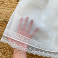 Dettaglio del tessuto a piccoli pois dell'abito battesimo neonata, con ricami floreali bianchi e bordo in pizzo smerlato.