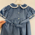 Dettaglio dell'abito bambina in velluto azzurro polvere con lavorazione smock, ricami panna e maniche corte con volant.